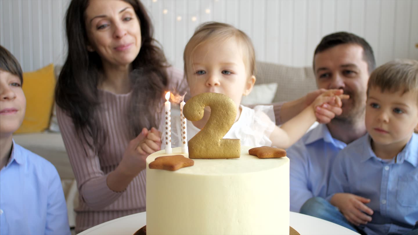 A second-birthday cake, candles lit, the family gathered round