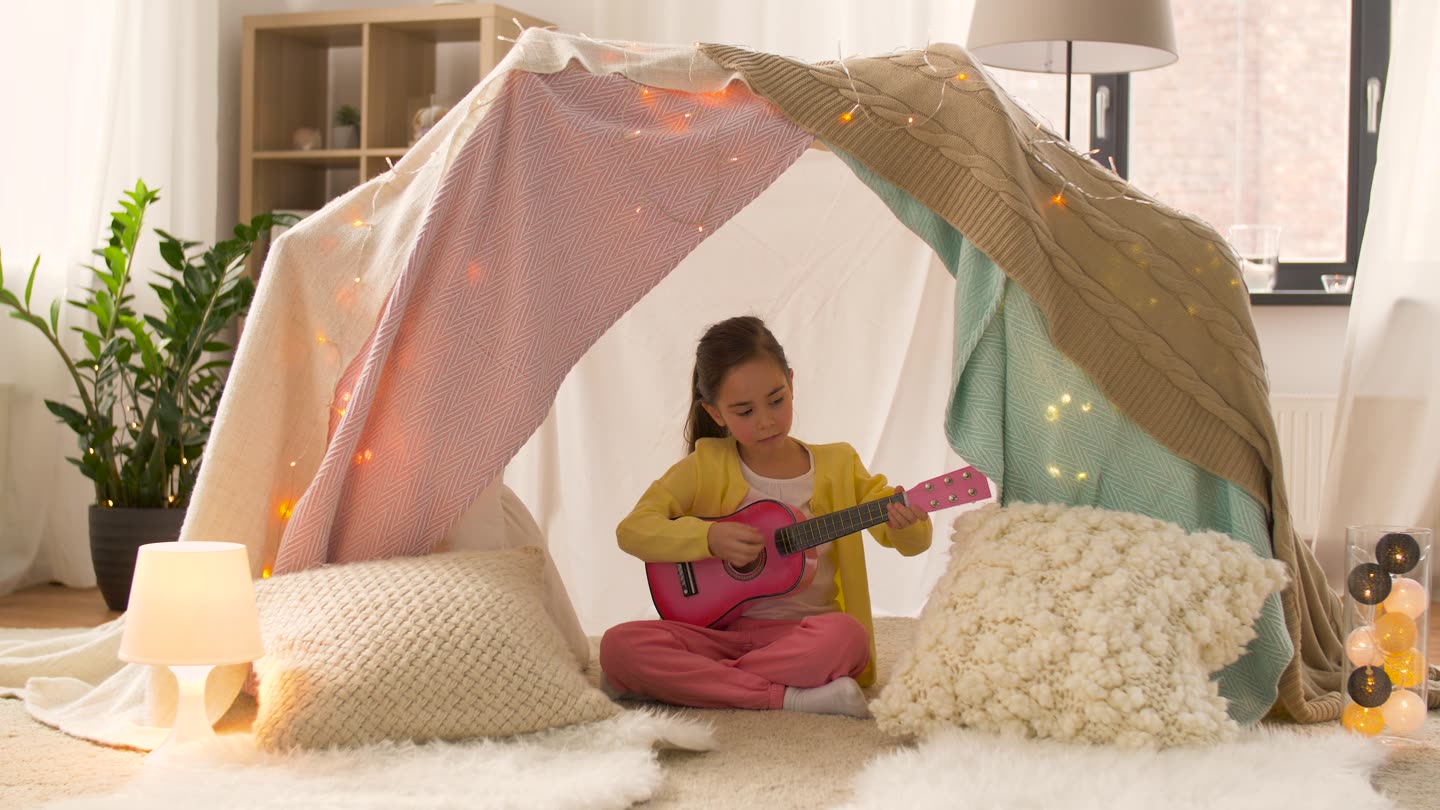 A girl playing guitar in a blanket den